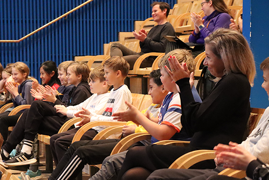 Avajaisiin osallistuneet koululaiset taputtavat esiintyjälle.