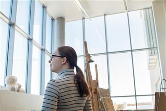 Opiskelija katselee ulos maalausateljeen korkeista ikkunoista. Kuva: Mari Parpala.