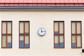 Kuva koulun seinästä, jossa näkyy neljä ikkunaa ja kello. 